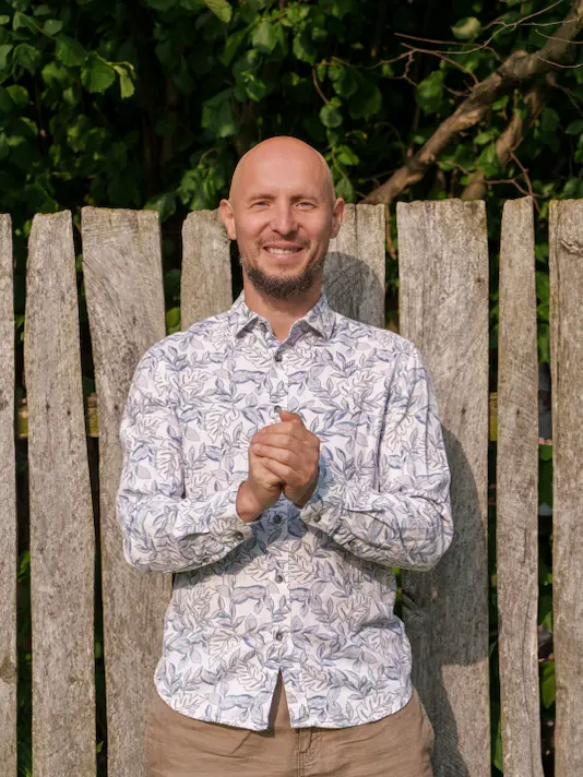 Krzysztof Lottig uśmiecha się i ma złączone ręce. Terapeuta i Muzyk